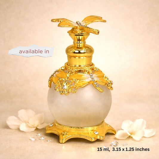 A decorative perfume bottle with a gold-toned floral cap and base, a frosted white spherical body, and gold floral embellishments with rhinestone accents. The bottle is centered on a beige background with decorative white flowers and text overlays reading 'available in' and '15 ml, 3.
