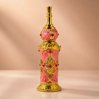 An ornate pink and gold perfume bottle with decorative filigree and red gem accents, centered on a warm beige background.