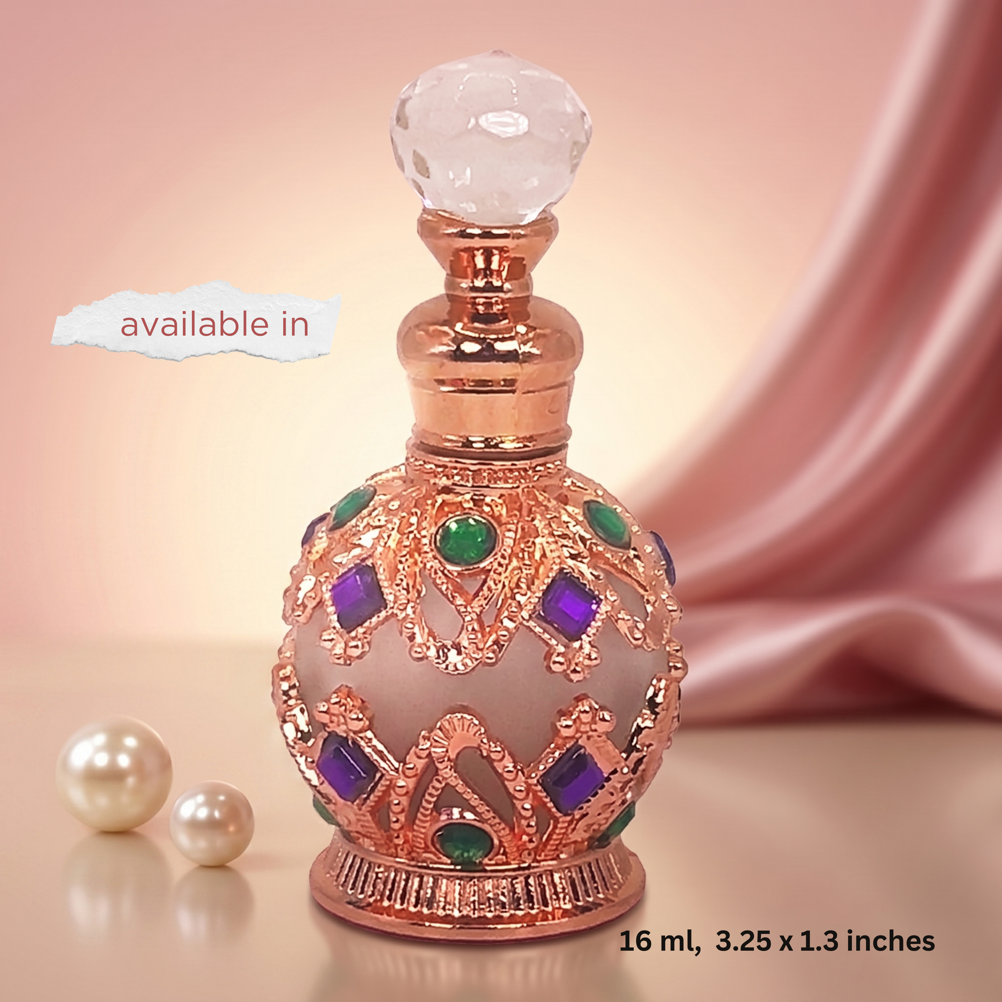 An ornate perfume bottle with a rose gold metallic body, a faceted clear glass stopper, and decorative green and purple gemstone accents, shown on a soft pink background with pearl props and a 'available in' label.